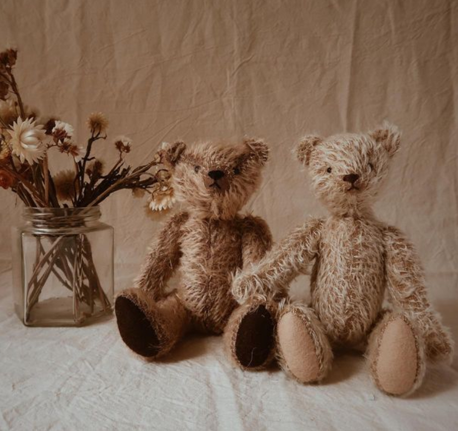 A pair of artist made OOAK mohair teddy bears sat next to a jam jar of dried flowers